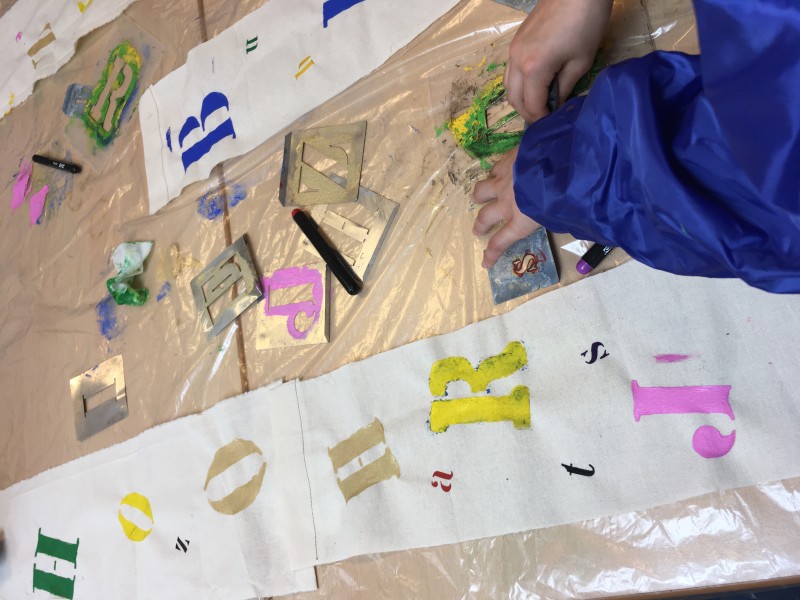 Kinderen bedrukken textiel met letters en verf.
