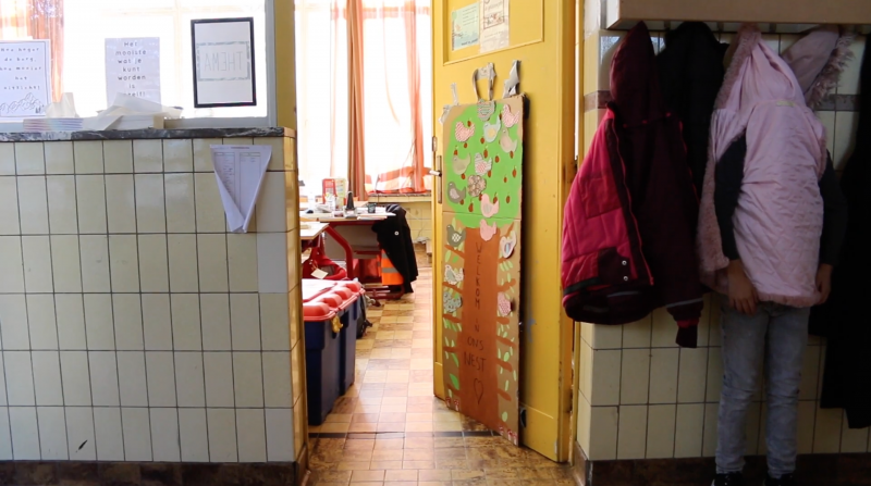 Kindje verbergt zich achter een jas aan de kapstokken in de gang