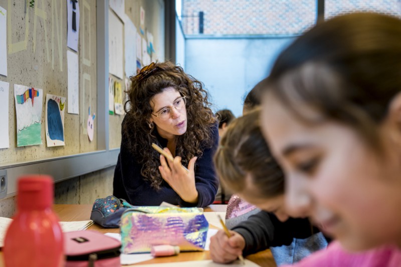 Kinderen in de klas met Inge Bogaerts aan tafel en potlood en papier